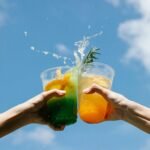 Two colorful cocktails clinked against a bright blue sky, celebrating summer in style.