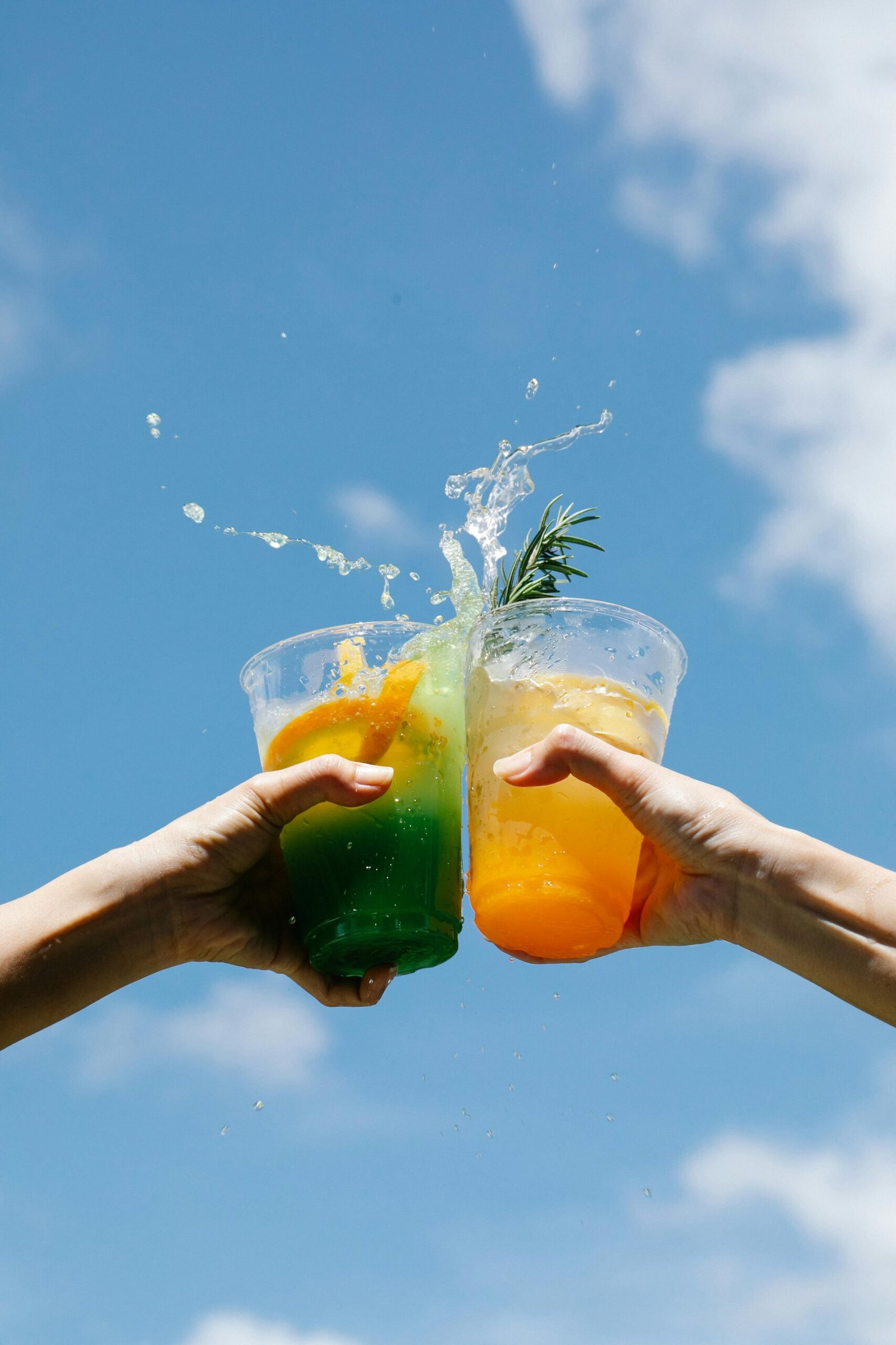 Two colorful cocktails clinked against a bright blue sky, celebrating summer in style.